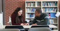 woman and man talking at table in library