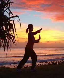 woman in front of sunset doing tai chi