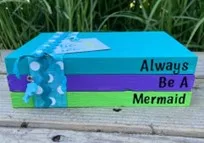 Farmhouse stacked books painted blue with text "Always Be a Mermaid"and ribbon