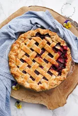 Pie with lattice top place on a wood tray surrounded by blue dish towel.