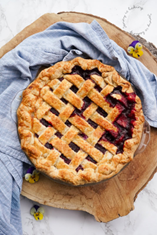 Pie with lattice top place on a wood tray surrounded by blue dish towel.